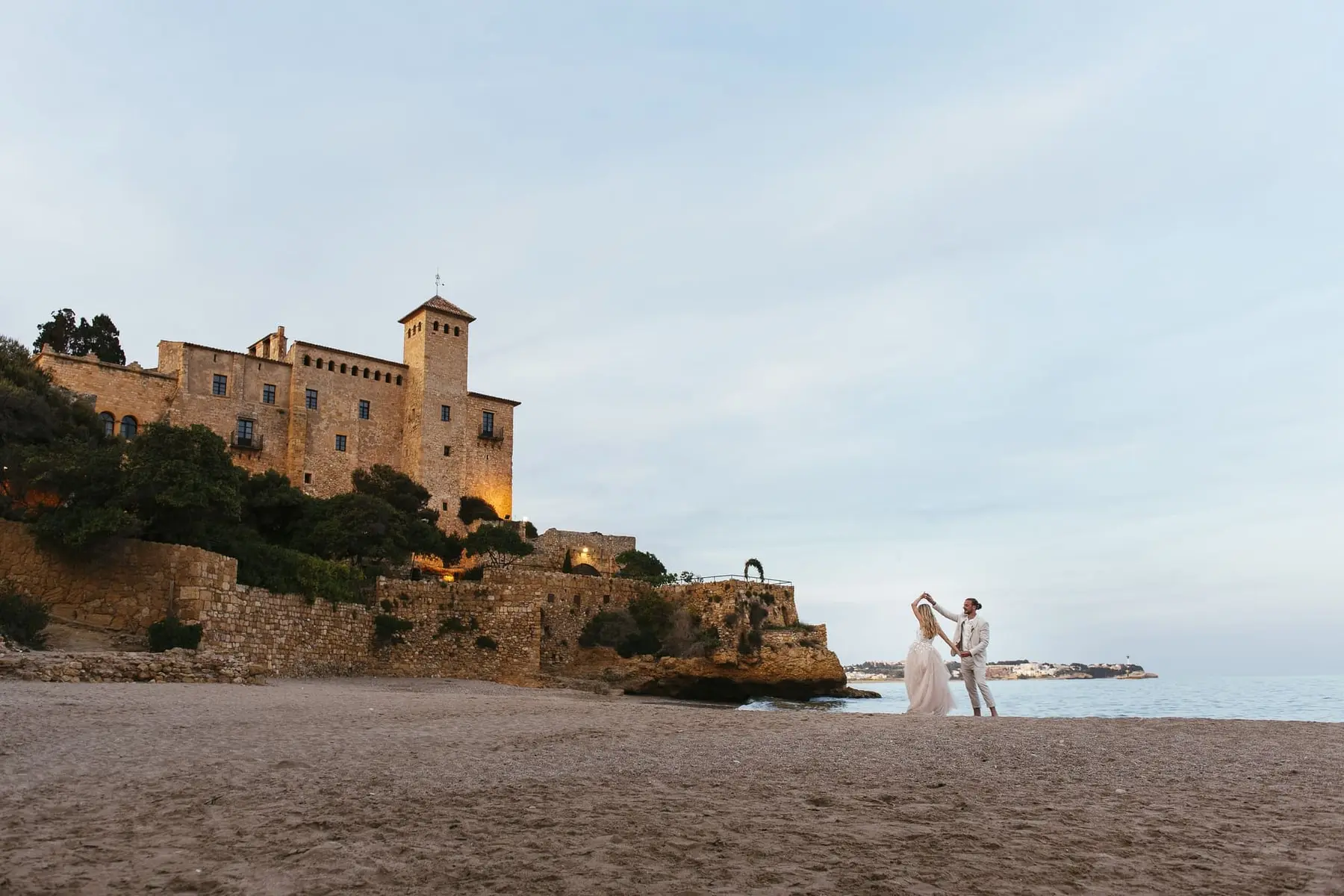 The couple dance on the beach with the castle behind
