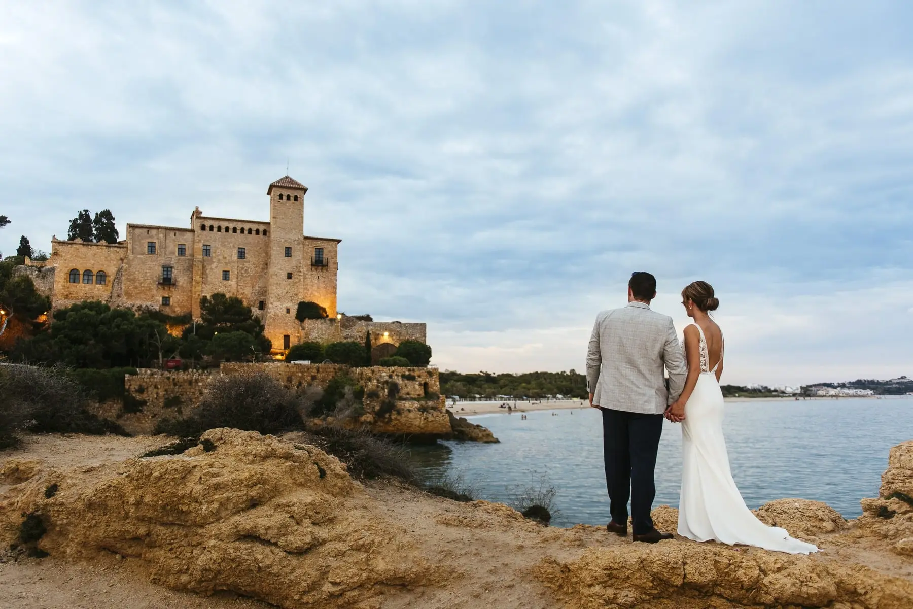 The couple hand in hand on the rocks, looking at the castle