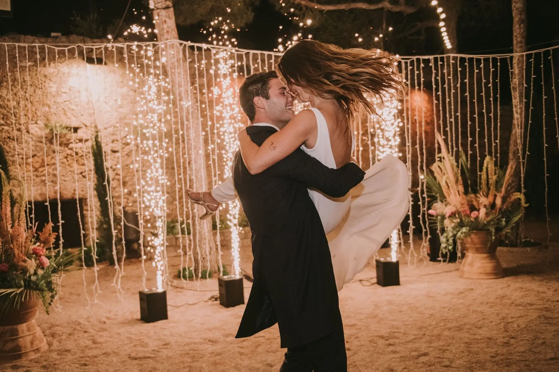 The groom lifts the bride beneath a curtain of lights